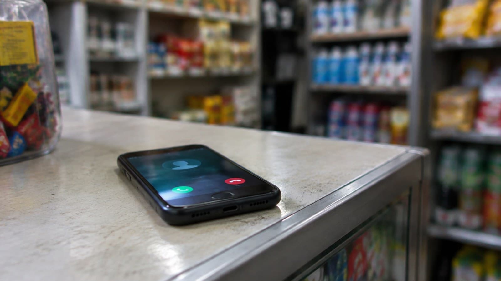 A smartphone lit with an incoming call on a shop counter, with shelves blurred behind